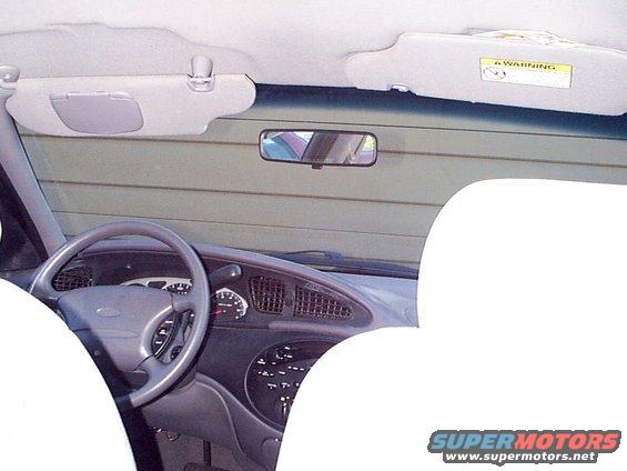 1999 Ford Taurus interior showing dashboard, steering wheel, and sun visors. Warning label visible on passenger sun visor
