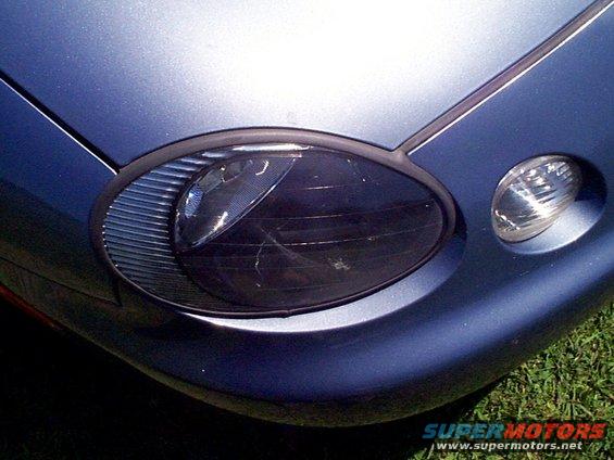 Blue car headlight with horizontal grille detail and amber marker light. Scratched lens