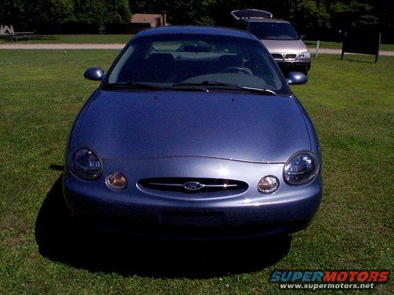 Front view of a blue 1999 Ford Taurus sedan parked on grass with another vehicle in the background