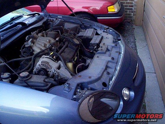 Engine bay of a 1999 Ford Taurus SE, with another red car behind it