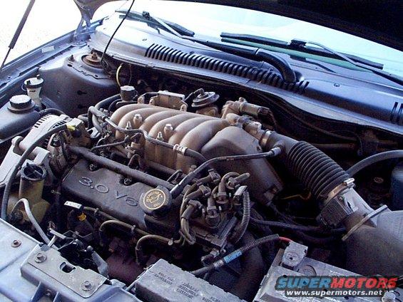 Engine bay of a 1999 Ford Taurus showing the 3.0 V6 engine with the hood open