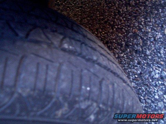 Close-up of a tire's tread pattern on a gravel surface. Supermotors.net logo visible