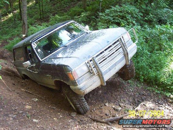 Dark blue Ford Bronco tilted on a muddy incline, front grille guard visible