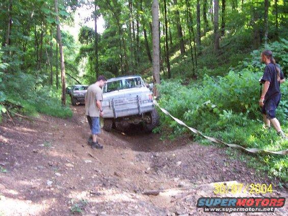 White Ford Bronco stuck on a dirt path in a forest, with a tow strap attached