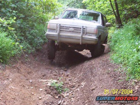 Light-colored SUV with brush guard driving off-road on a dirt path