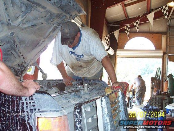 Two guys working on the engine of a truck in a garage. Racing flags hang overhead