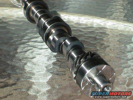 Camshaft with lobes and a gear at the end, resting on a textured surface