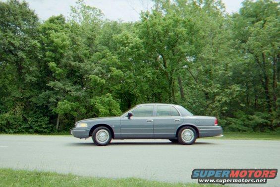 Gray 1998 Ford Crown Victoria sedan parked on asphalt road with trees in background