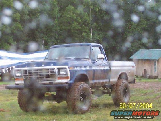 Blue and silver Ford pickup truck with lifted suspension and large tires, seen from the front-right