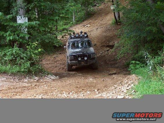 Black SUV with roof lights driving down a dirt trail in the woods