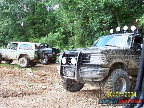 Mud-covered 1995 Ford Bronco in foreground, with two other Broncos behind it on a dirt trail