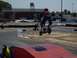 1990 Ford Bronco - Rider on a scooter takes flight over a ramp during a race event. Other participants are visible on the track.