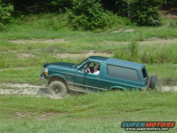 Green 1995 Ford Bronco driving through mud