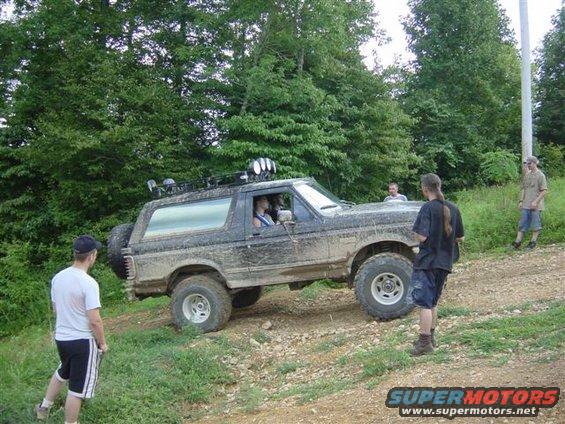 Muddy Ford Bronco on a dirt path with people around