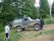 1995 Ford Bronco - A group of people stand around a dirty Ford Bronco as it navigates an off-road trail.