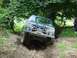 1995 Ford Bronco - 1995 Ford Bronco tackling an off-road trail. The vehicle is tilted as it climbs a muddy, rutted path.