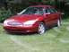 2000 Ford Taurus - Red 2000 Ford Taurus sedan parked on a grassy area with trees in the background.