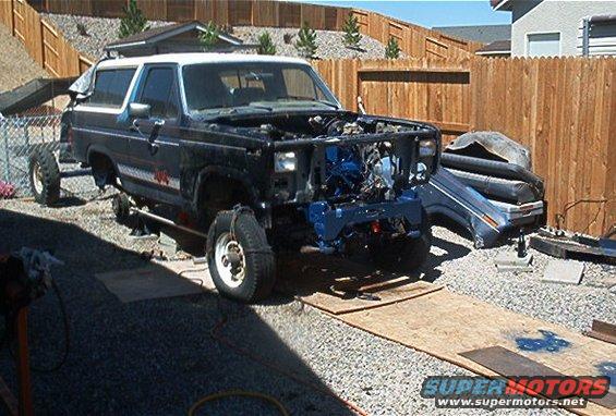 Ford Bronco with front end removed, engine exposed, on jack stands in a driveway