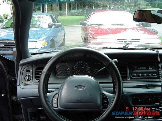 Interior view of a blue car, showing dashboard and steering wheel. Two other cars, a red and a blue sedan, are visible through the windshield