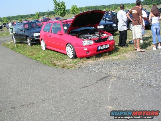 Red hatchback car with white rims and hood open, showing engine. License plate EAH-036