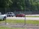 1990 Jeep YJ - An orange hatchback is parked behind a chain-link fence, with other vehicles visible in the background.