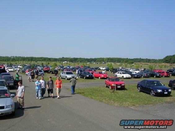 Outdoor car show with many cars parked on grass and asphalt under a clear blue sky