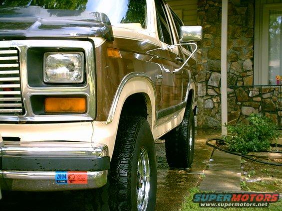 Brown and tan Ford Bronco front quarter view, chrome grille, square headlights, two stickers on bumper