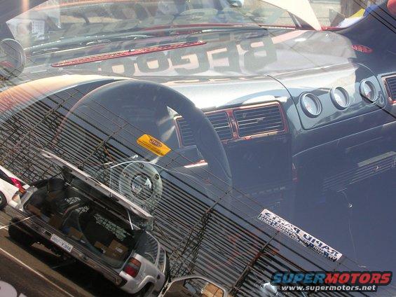 Interior view with dashboard and steering wheel, reflection of a silver SUV with open trunk