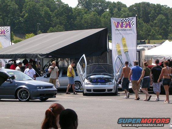 Silver Volkswagen Golf GTI with doors open, parked next to a dark grey car. People walk by
