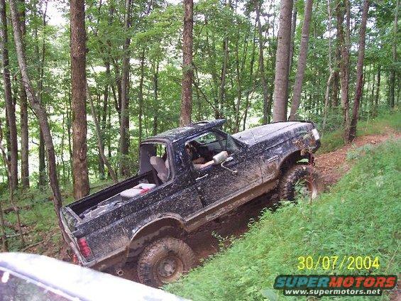 Mud-covered black 1992 Ford Bronco climbing a dirt path in a forest