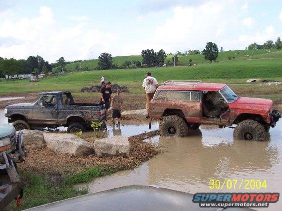 Mud-splattered black Ford Bronco stuck in mud, viewed from the front-left