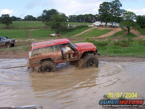 Red SUV stuck in mud pit, another vehicle visible in background