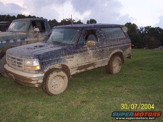 Mud-covered 1995 Ford Bronco parked on grass next to another truck
