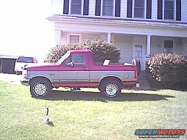 Red and grey two-door pickup truck parked on grass, side view