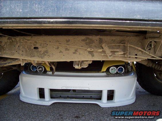 Yellow car's front bumper and headlights are visible underneath a larger vehicle
