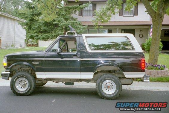 Side view of a black and white 1993 Ford Bronco with a roof rack and aftermarket wheels
