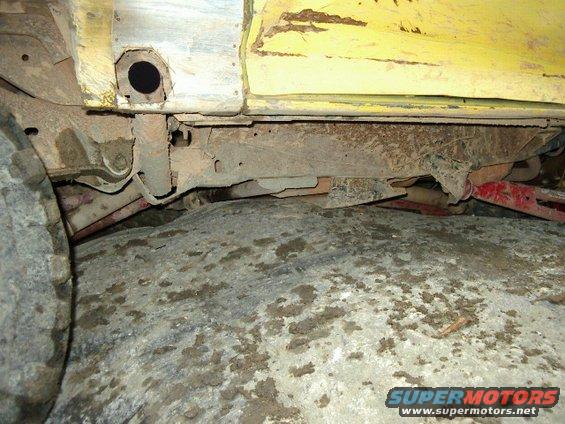 Yellow vehicle frame and tire, showing rust and dirt on the undercarriage