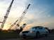 2000 Ford Crown Victoria - A white 2000 Ford Crown Victoria is parked near a construction site with large cranes silhouetted against the sunset sky.
