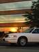 2000 Ford Crown Victoria - A white 2000 Ford Crown Victoria is parked in front of a building whose windows reflect a vibrant sunset.