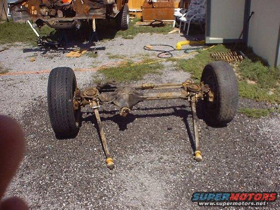 front axle assembly with two wheels on gravel, vehicle frame in background