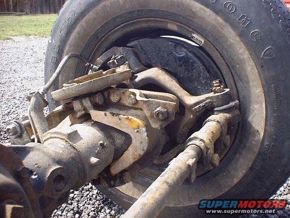 Front axle assembly with brake drum and suspension components, showing rust and wear