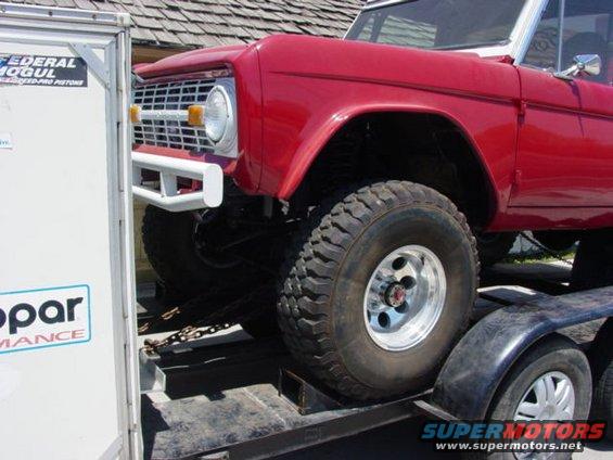 Red Ford Bronco with white grille and bumper on a trailer, side view
