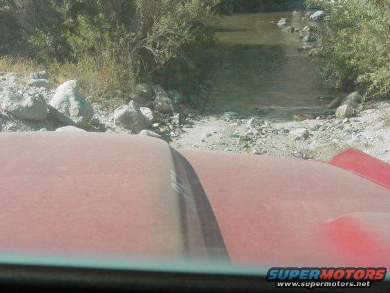 Red SUV hood driving through a rocky stream