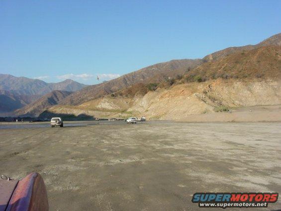 Several SUVs parked and driving on a dirt road with mountains in the background