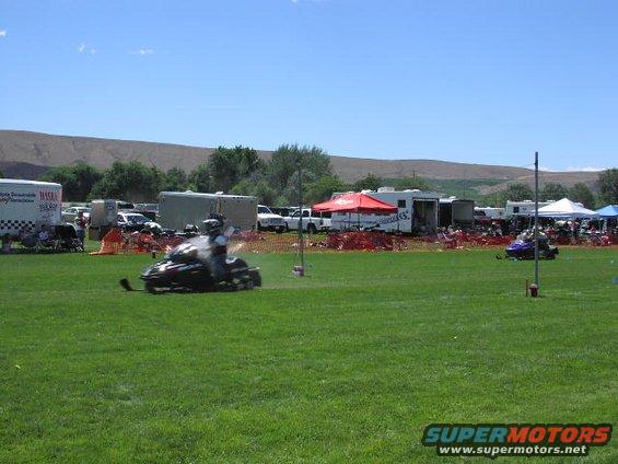 Snowmobile racing on a grassy field with trailers and tents in the background