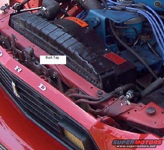 Close-up of a red car's engine bay showing the radiator and a label pointing to a 'Buck Tag'