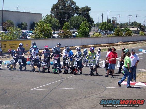 Row of mini bikes with riders in racing gear at a starting line