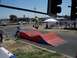 1990 Ford Bronco - A scooter rider performs a jump over a ramp at an outdoor event with spectators and tents in the background.