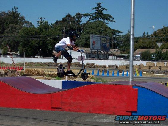 Person on gas scooter jumping over ramp at outdoor track