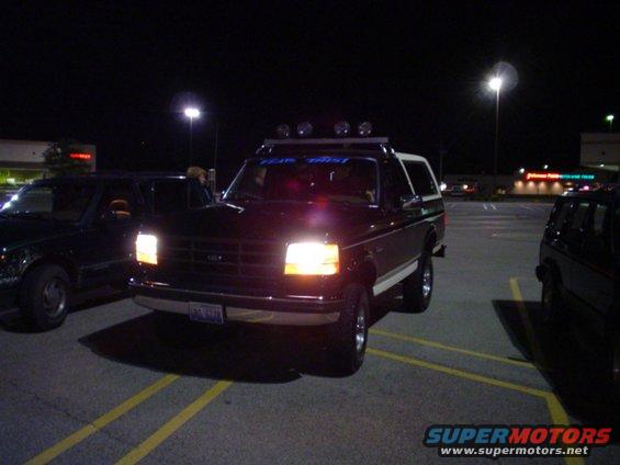 1993 Ford Bronco parked in a parking lot at night, front view. Another vehicle is parked to the left
